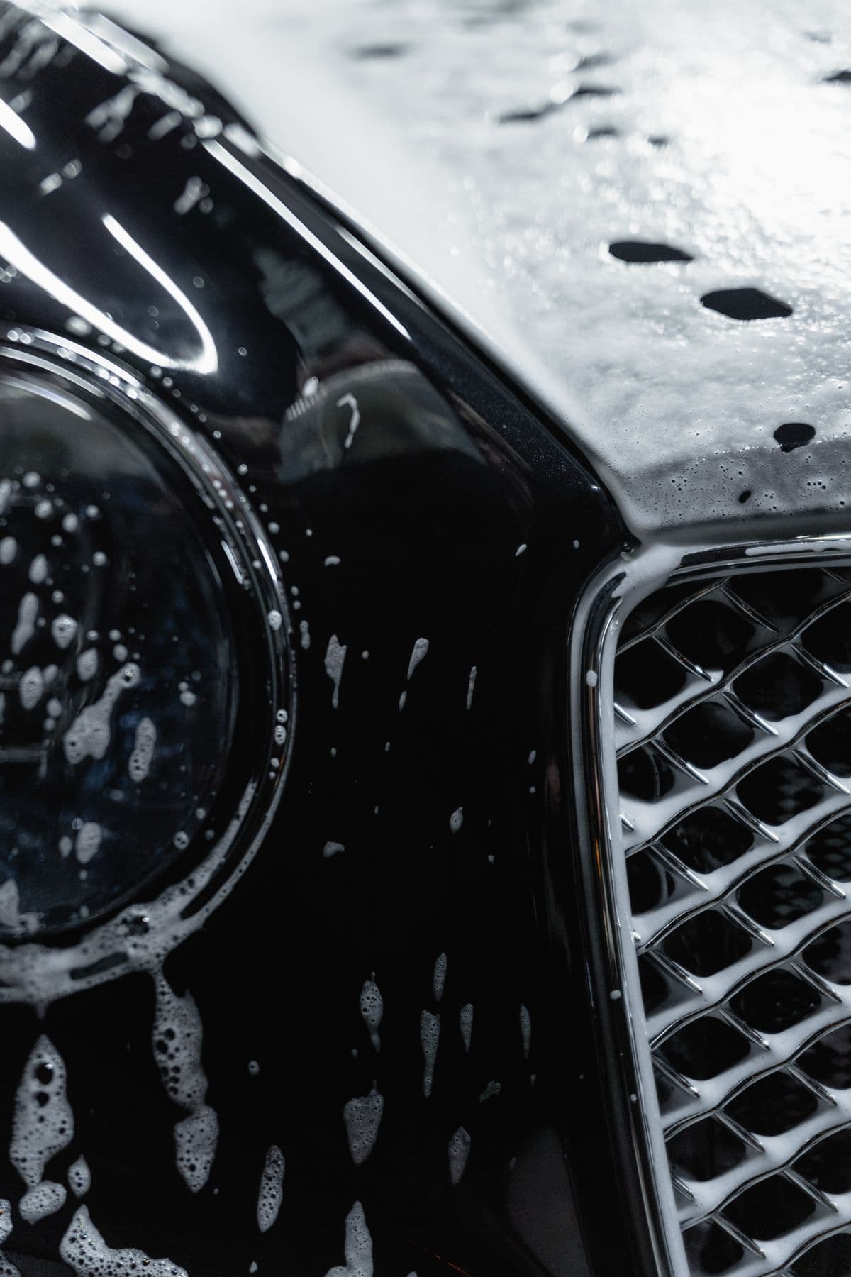 Dark luxury sedan covered in cleaning foam during an exterior hand wash