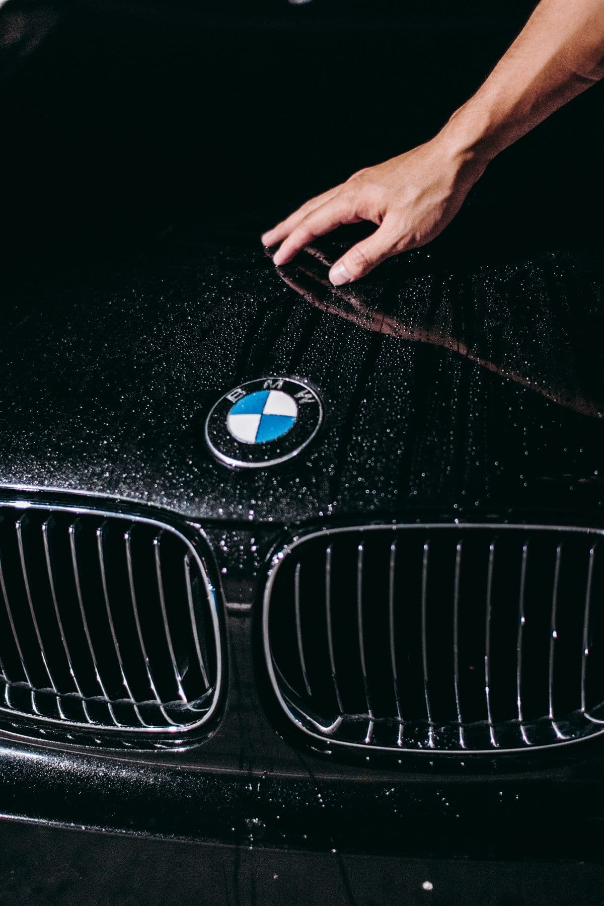 Close-up of a hand wiping a clean car hood with water droplets beading on the paint