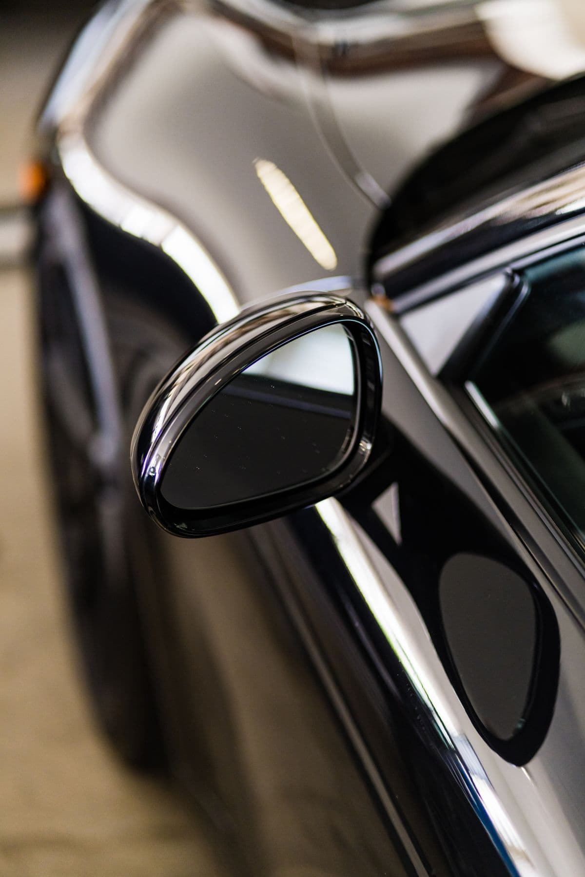 Close-up of a glossy black car side mirror reflecting its surroundings after detailing