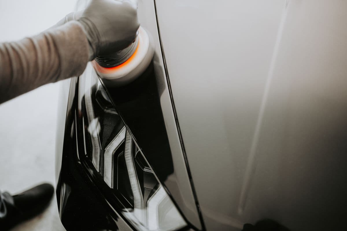 Hand guiding a dual-action polisher with an orange pad across a glossy black car panel