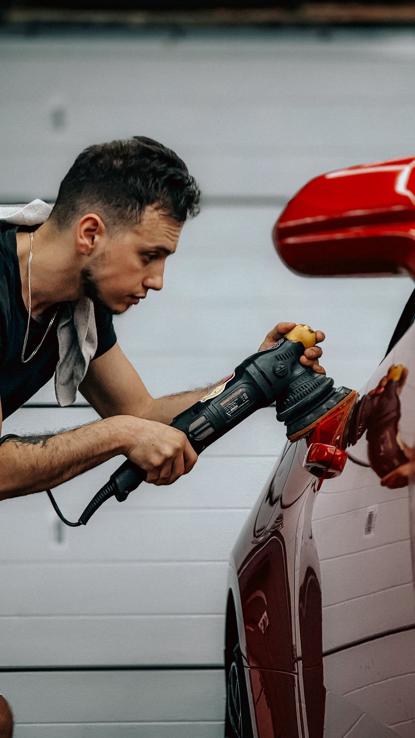 Detailer machine-polishing the painted panel of a red car to remove swirl marks